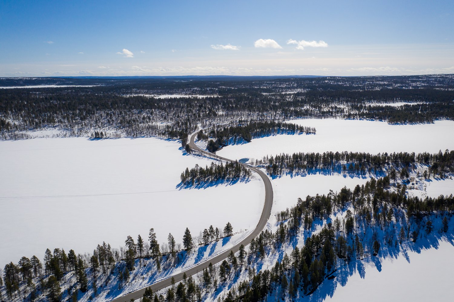 Ilmakuva talvisesta maisemasta, missä näkyy järviä, metsää ja tie.